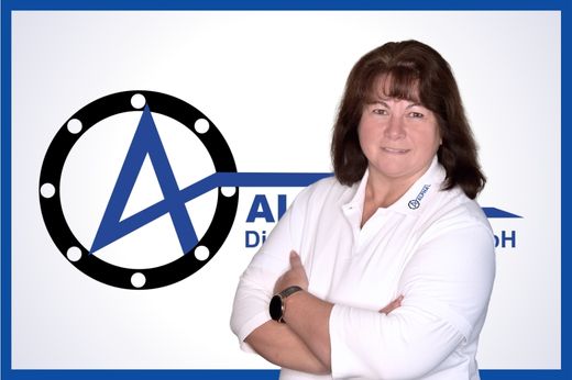 Auftragsbearbeitung Ramona Mederake mit verschränkten Armen mit weißem Hemd vor dem blauen Alpha-Logo auf weißem Hintergrund.
